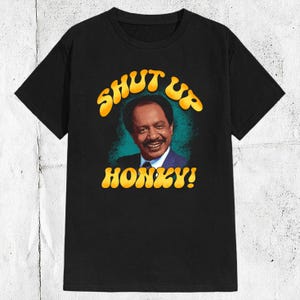 Könnte beinhalten: Schwarzes T-Shirt mit einer gelben Grafik eines Mannes mit dem Text "Shut Up Honky!"