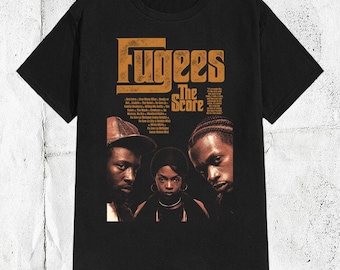 Op de afbeelding: Een zwart t-shirt met korte mouwen en een grafische print van het Fugees-album The Score. Het ontwerp bevat de bandnaam in grote oranje letters, een tracklist en een fotografisch portret van de drie leden in bruintinten.