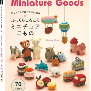 以下が含まれることがあります： 刺しゅう糸で編むかぎ針編み ふっくらころころ ミニチュア こもの (刺繍糸で編むかぎ針編み ふっくらころころ ミニチュア こもの) と題された、70種類のあみぐるみパターンを収録した本の表紙。表紙には、動物、食べ物、乗り物など、さまざまなカラフルなあみぐるみが描かれています。