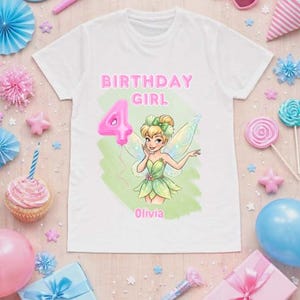 May include: A white short-sleeved t-shirt featuring a graphic of a fairy with green wings, a pink balloon shaped like the number 4, and the text "BIRTHDAY GIRL" and "Olivia" printed in pink on a light green watercolour-style background.