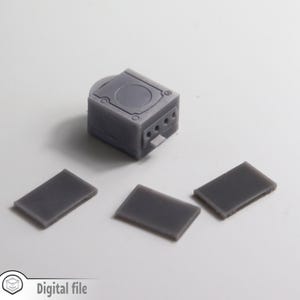 May include: A gray 3D printed model of a GameCube console with three gray controllers.