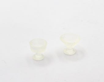 May include: Two clear glass cups with a pedestal base. The cups are small and appear to be made of a translucent material.