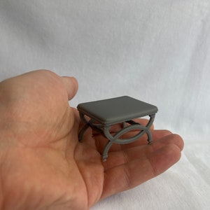 May include: A small gray table with a square top and intricate, curved legs. The table is made of a smooth, matte material and appears to be made of plastic or resin.
