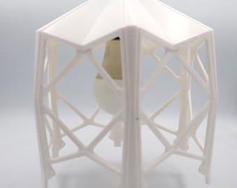 Pode incluir: Luminária pendente geométrica branca com uma lâmpada branca pendurada dentro. A luminária é feita de um design de treliça impresso em 3D.