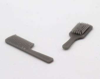 Op de afbeelding: Twee grijze plastic haarverzorgingstools: een kam en een borstel. De kam heeft fijne tanden en een lange steel. De borstel heeft een rechthoekige kop met borstelharen en een lange steel.