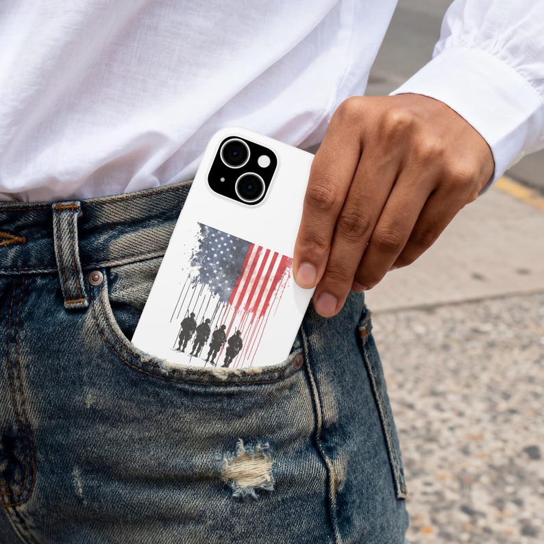 May include: White phone case featuring an American flag design with a silhouette of soldiers. The flag is depicted with red and white stripes and a blue field of stars. The case is in a pocket.