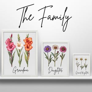 Three framed prints on a white shelf, with a large print of gladiolus labeled "Grandma," a medium print of asters labeled "Daughter," and a small print of daisies labeled "Grand-daughter," with "The Family" written above.