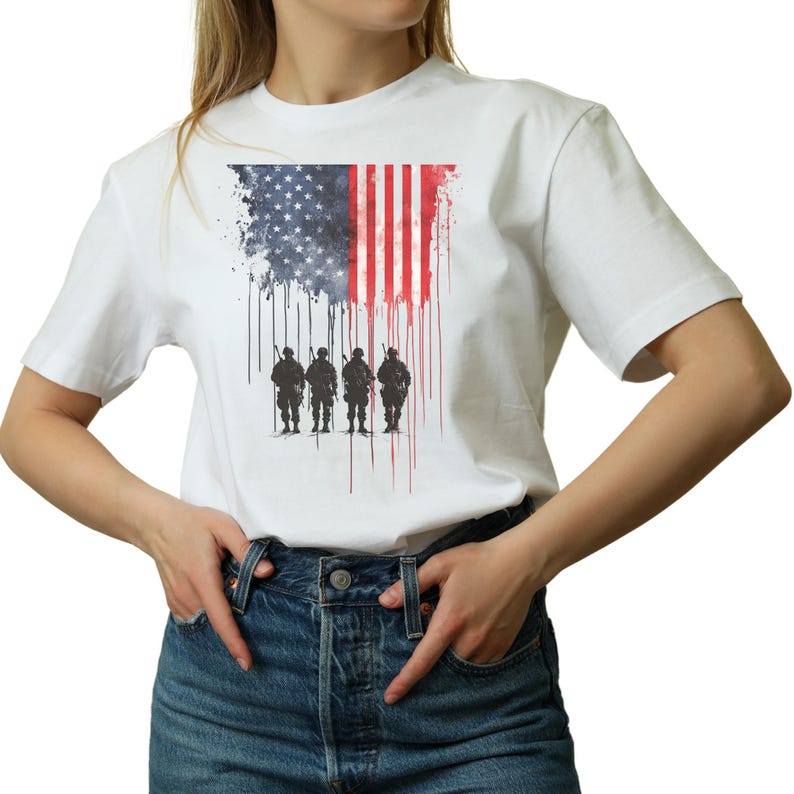 May include: White t-shirt featuring a graphic of the American flag with a distressed effect and silhouettes of soldiers. The flag design incorporates the stars and stripes, with a dripping paint effect. The shirt is a classic crew neck style.