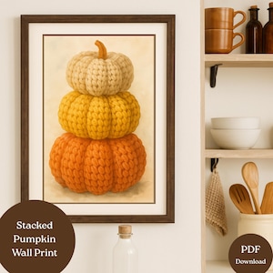 May include: A framed wall print depicting a stack of three knitted pumpkins in cream, yellow, and orange. The pumpkins are arranged vertically, with a brown frame and a neutral background. The print is labeled "Stacked Pumpkin Wall Print."