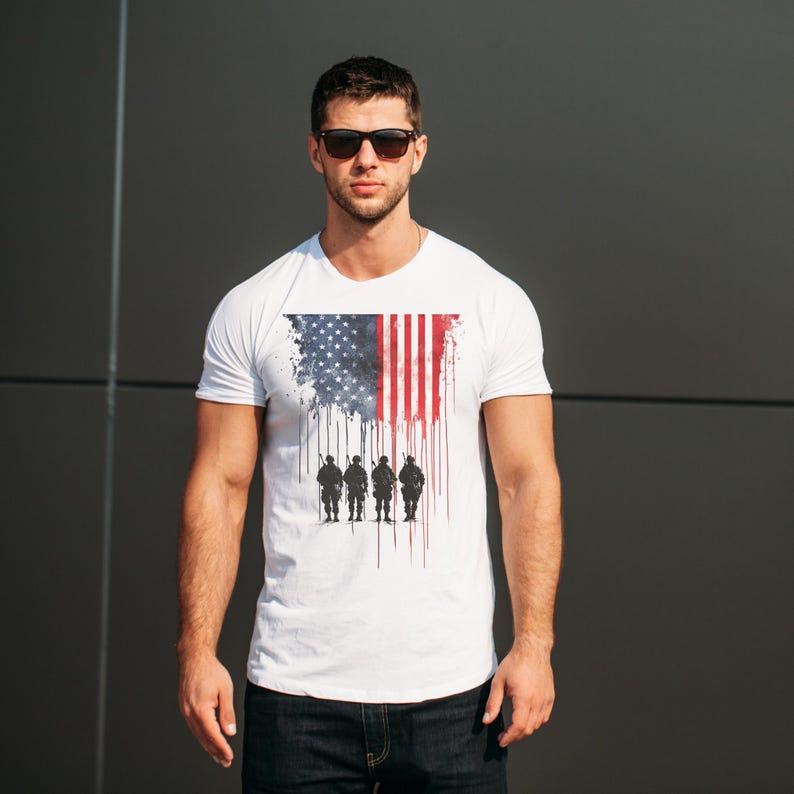 May include: White t-shirt featuring a distressed American flag design with a silhouette of soldiers. The flag design incorporates the stars and stripes in shades of blue, red, and white. The shirt is a classic crew neck style.