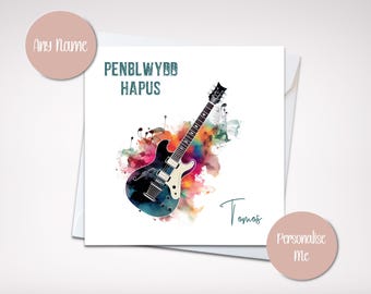 Puede incluir: Una tarjeta de felicitación blanca con una ilustración de acuarela de una guitarra eléctrica en blanco y negro. La tarjeta tiene las palabras "PENBLWYDD HAPUS" y "Tomos" escritas. Hay dos círculos rosas con las palabras "Any Name" y "Personalise Me".