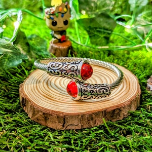 May include: A silver bangle bracelet with a twisted design and two red gemstone accents.