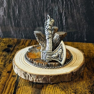 以下が含まれることがあります： 木製の台座に置かれた、複雑なディテールと狼のデザインが施された銀製の斧のペンダント