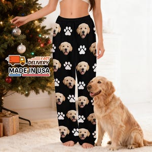 Pode incluir: Calças de pijama pretas com um padrão repetido de rostos de golden retriever e pegadas brancas. As calças têm uma cintura com cordão. As palavras "FAST DELIVERY" e "MADE IN USA" são visíveis em um letreiro.