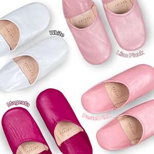Puede incluir: Cinco pares de zapatillas de cuero en diferentes colores: blanco, rosa lila, magenta, rosa pastel. Las zapatillas son todas del mismo estilo, con punta puntiaguda y parte trasera cerrada.