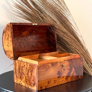 Könnte beinhalten: Eine Holzkiste mit einem Scharnierdeckel und einem Messingverschluss. Die Kiste ist aus dunklem Holz mit natürlicher Maserung. Die Kiste ist geöffnet und der Innenraum ist leer.