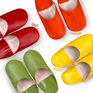 Puede incluir: Cuatro pares de zapatillas de cuero en diferentes colores: rojo, naranja, verde y amarillo. Cada par tiene la palabra "HERIMA" impresa en el interior.