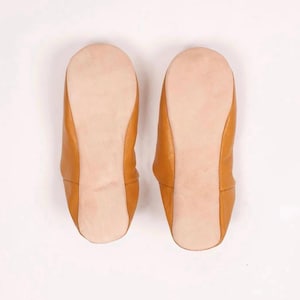 Puede incluir: Un par de zapatillas de cuero marr&oacute;n con un forro suave de gamuza. Las zapatillas tienen una punta redonda y un dise&ntilde;o simple y minimalista.