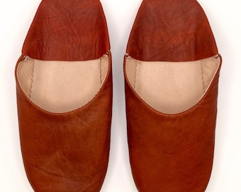 May include: A pair of brown leather slippers with a soft, beige lining. The slippers have a simple, classic design and are perfect for relaxing at home.