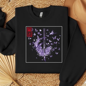 May include: Black sweatshirt with a purple and white graphic of a katana sword surrounded by butterflies. The Japanese word "鬼滅" is printed in red on the left side of the graphic.