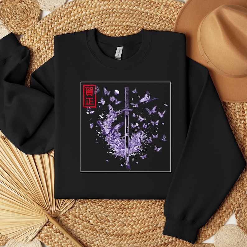 May include: Black sweatshirt with a purple and white graphic of a katana sword surrounded by butterflies. The Japanese word "鬼滅" is printed in red on the left side of the graphic.