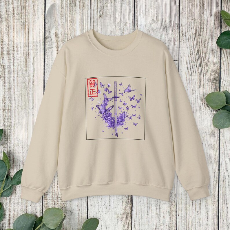 May include: A beige sweatshirt with a graphic print of a sword surrounded by purple butterflies. The graphic also includes a red square with Japanese characters that read "正" (sei).