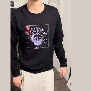 May include: Black long-sleeve sweatshirt with a graphic print of a sword surrounded by purple butterflies. The graphic also includes the text "悟" in red.