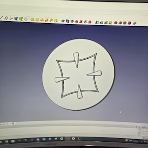 Puede incluir: Una pantalla de ordenador que muestra un diseño de una cruz blanca dentro de un círculo sobre un fondo gris.