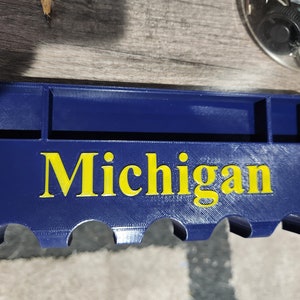 Puede incluir: Un organizador de plástico azul con la palabra "Michigan" en letras amarillas. El organizador tiene cinco ranuras y un pequeño compartimento en el centro.