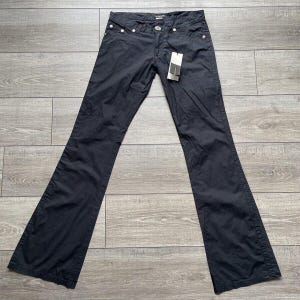 Può includere: Pantaloni neri a zampa d'elefante con un bottone e rivetti argentati. I pantaloni hanno un'etichetta attaccata alla cintura.