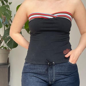 May include: Black tube top with a colorful striped band at the top. The top has the word "elle" in red script on the front. The model is wearing dark blue denim jeans.