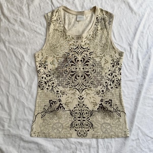 May include: Cream-coloured sleeveless top with a brown and tan floral pattern. The tank top features a scoop neck and a decorative design that covers the entire front. The brand tag is visible at the neckline.