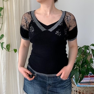 May include: Black short-sleeved top with a V-neck and a ribbed texture. The sleeves and neckline are trimmed with silver and sheer black lace. The top is paired with a denim mini skirt.
