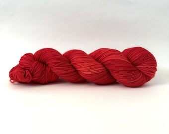May include: A skein of red yarn with a subtle ombre effect. The yarn is soft and smooth, and it is perfect for knitting or crocheting.