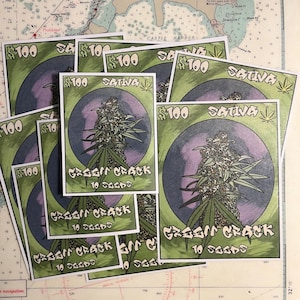 Peut inclure: Une pile d'autocollants verts et violets avec le texte "$100 SATIVA GREEN CRACK 10 SEEDS" dessus.