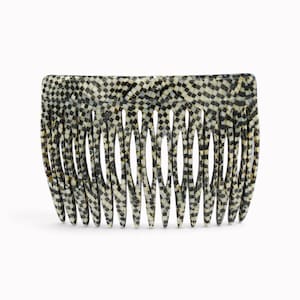 Pode incluir: Um pente de cabelo com um padrão xadrez repetitivo em preto, branco e dourado. O acessório tem uma borda superior curva e vários dentes afilados projetados para pentear, com um acabamento polido e um design detalhado de grade geométrica.