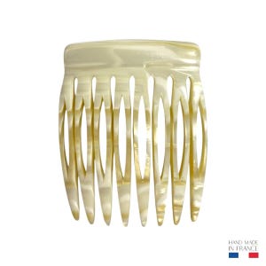 May include: A cream-coloured hair comb with a marbled effect. The comb has a curved top and a series of evenly spaced teeth. The comb is made of a glossy material and is suitable for various hair types. The comb is handmade in France.