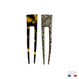 Puede incluir: Dos horquillas para el cabello. Una tiene un patrón de carey con tonos negros, marrones y amarillos. La otra tiene un diseño a cuadros en blanco y negro. Ambas tienen un recorte en forma de U en la parte superior.