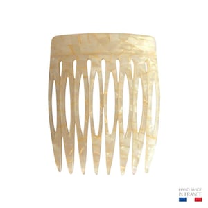 Peut inclure: Un peigne à cheveux crème avec un design en forme d'ovale. Le peigne présente un motif texturé en mosaïque avec une finition brillante. Le peigne est fabriqué à la main en France.