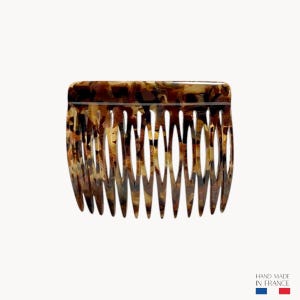 Könnte beinhalten: Ein Haarkamm mit Schildpattmuster mit gewölbter Oberseite und gleichmäßig verteilten Zähnen. Der Kamm besteht aus braunem und beigem Material. Das Bild enthält den Text "HAND MADE IN FRANCE".
