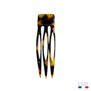 Könnte beinhalten: Ein Haarkamm im Schildpattmuster mit vier Zinken. Der Kamm hat eine rechteckige Oberseite und besteht aus einem glänzenden, dunkelbraunen und gelben Material. Der Text "HAND MADE IN FRANCE" ist unten rechts sichtbar.