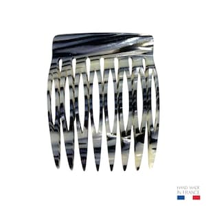 Peut inclure: Un peigne à cheveux avec un motif marbré noir, blanc et gris. Le peigne a une série de dents incurvées et un dessus arrondi. Fabriqué à la main en France.