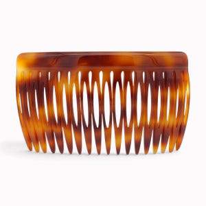 Könnte beinhalten: Ein breiter Haarkamm mit klassischem Schildpattmuster und einer glatten, glänzenden Oberfläche. Das Accessoire hat eine geschwungene Oberkante und zahlreiche lange, schmale, gleichmäßig angeordnete Zinken zur Haarfixierung.
