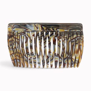 May include: A hair comb featuring a marbled pattern in shades of brown, white, yellow, and black. The accessory has a curved top edge and a series of long, tapered teeth designed for styling hair, with a smooth, polished finish throughout.