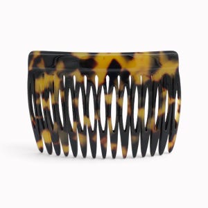 Könnte beinhalten: Ein Haarkamm mit klassischem Schildpattmuster in einer Mischung aus dunkelbraunen, schwarzen und bernsteinfarbenen Tönen. Das Accessoire hat eine glatte, geschwungene Oberkante und eine Reihe von elf langen, spitz zulaufenden Zinken.
