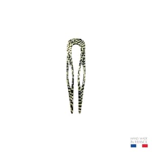 Puede incluir: Una pinza para el pelo a cuadros en blanco y negro. El accesorio para el cabello tiene forma de U larga y delgada con un patrón decorativo. La pinza está hecha de un material brillante y está sobre un fondo blanco.