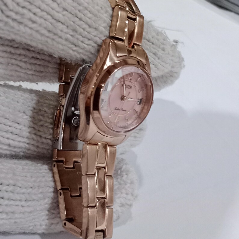 Puede incluir: Reloj de pulsera de color oro rosa con esfera rosa y visualizaci&oacute;n de la fecha. El reloj presenta un brazalete de eslabones y una esfera redonda con la marca "SVICA". Un accesorio cl&aacute;sico.