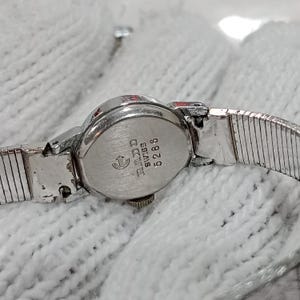 Op de afbeelding: Een vintage zilverkleurig Rado horloge met een zilveren band. De wijzerplaat is ovaal met de merknaam en "Swiss" op de achterkant. De horlogeband heeft een flexibel, geribbeld ontwerp.