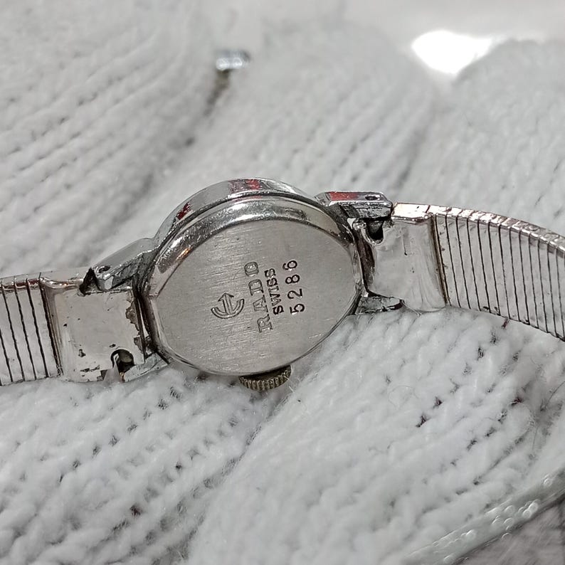 Op de afbeelding: Een vintage zilverkleurig Rado horloge met een zilveren band. De wijzerplaat is ovaal met de merknaam en "Swiss" op de achterkant. De horlogeband heeft een flexibel, geribbeld ontwerp.