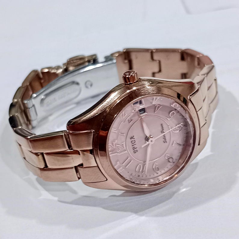 Puede incluir: Un reloj Spiga en oro rosa con una correa a juego. La esfera del reloj es de color rosa claro con n&uacute;meros romanos y las palabras "Solar Power". La correa est&aacute; hecha de eslabones rectangulares.
